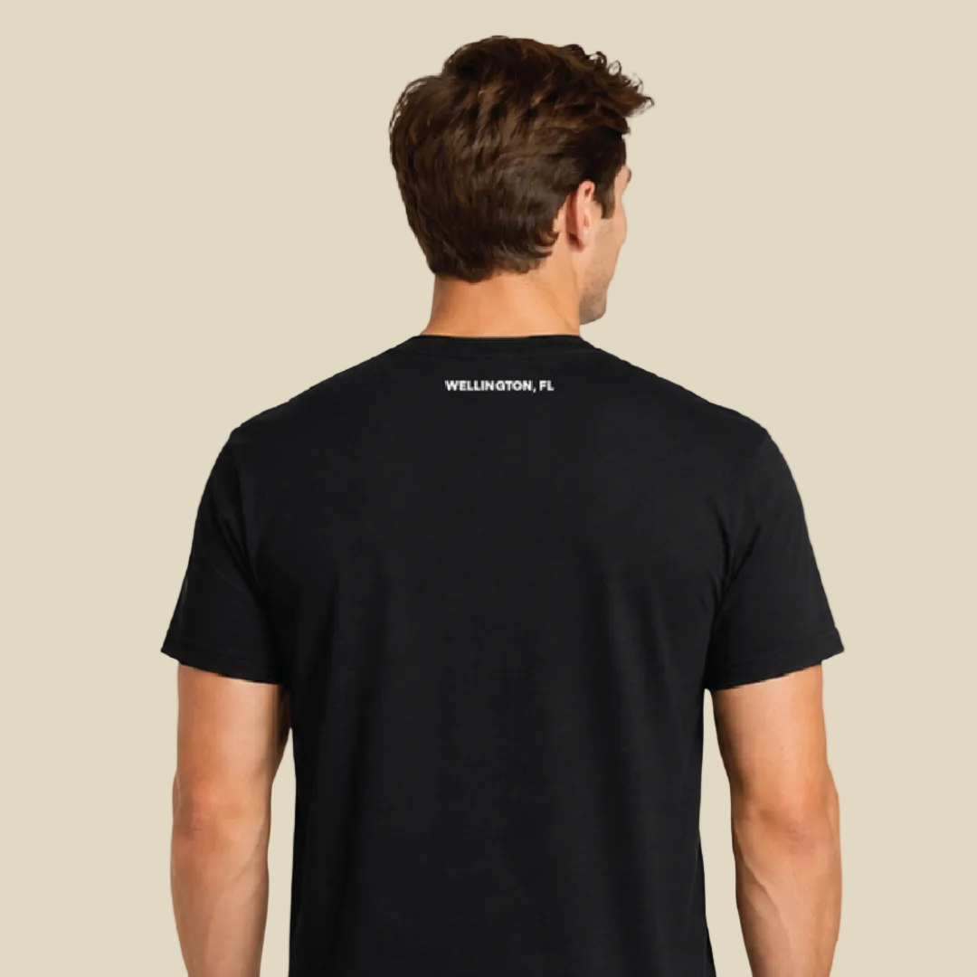 A man viewed from the back wearing a black short-sleeve t-shirt with 'WELLINGTON, FL' printed in white text on the upper back, set against a tan background.