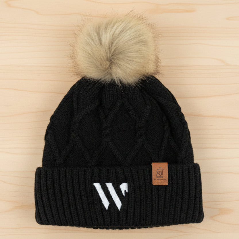 Black knit beanie with a beige pom-pom on a wooden surface