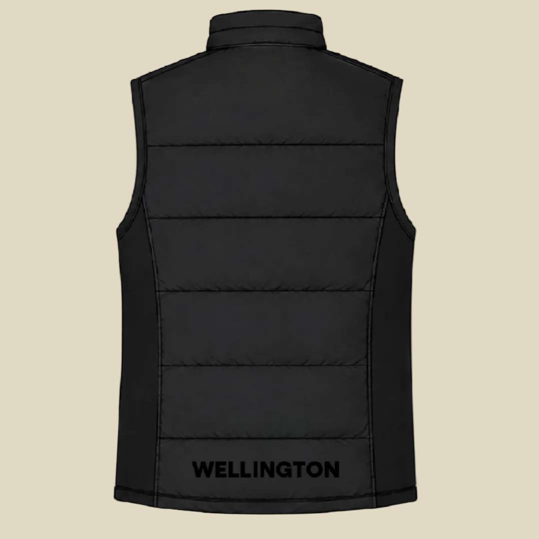 Black sleeveless puffer vest shown from the back, featuring horizontal quilting and the brand name WELLINGTON printed in black near the bottom hem, set against a tan background.