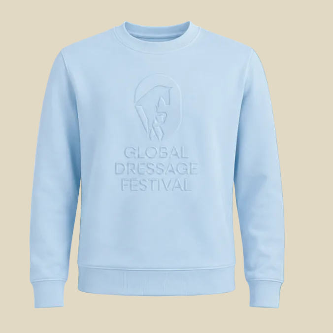 A light blue crewneck sweatshirt featuring an embossed tonal graphic of a horse rider and the text 'GLOBAL DRESSAGE FESTIVAL' on the chest, displayed against a solid tan background.