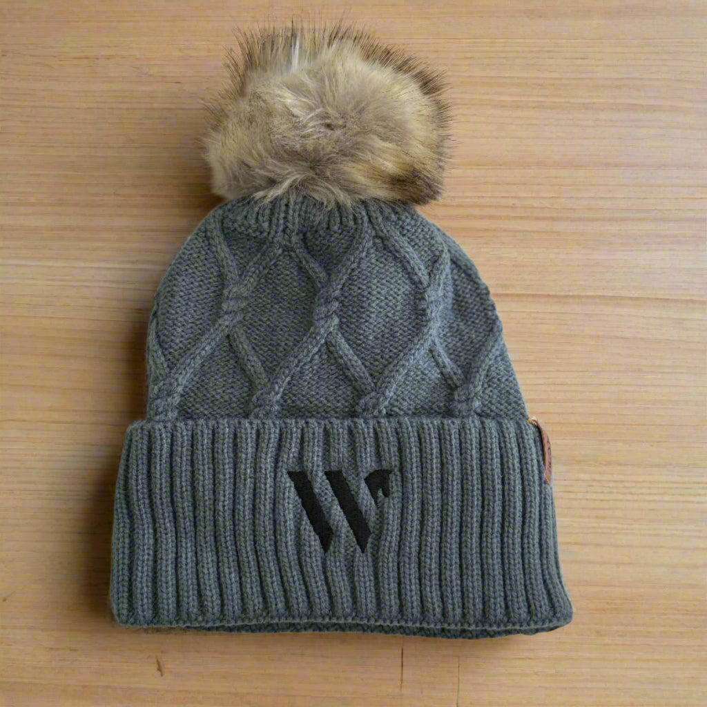 Gray knit beanie with a fur pom-pom on a wooden desk background