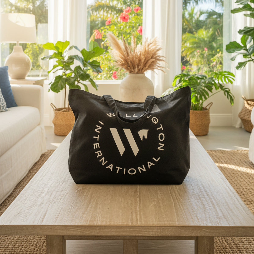 A black fabric tote bag with a white circular 'WELLINGTON INTERNATIONAL' logo printed on the front, displayed in a home.