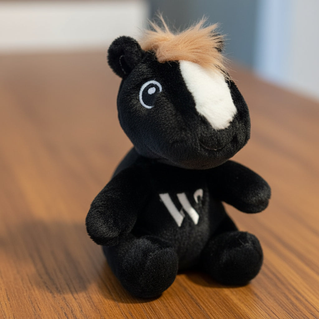 Black plush toy keychain with a white patch on a wooden table