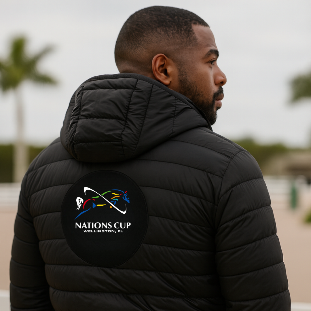 Man wearing a black puffer jacket with dressage Nations Cup'logo on the back, standing outdoors.